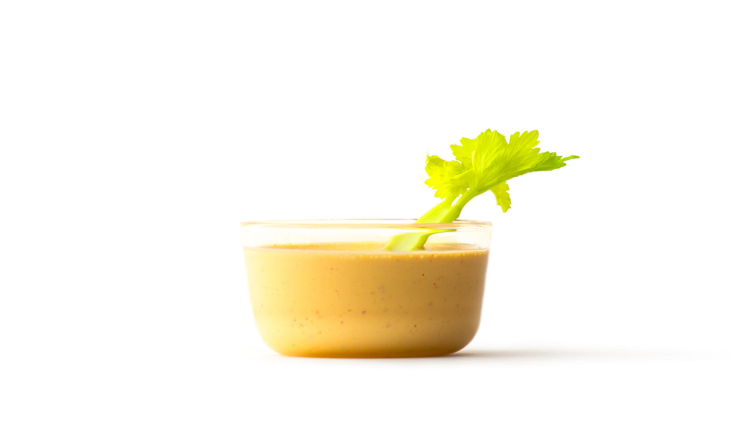 cashew aioli in a clear round bowl with a celery stalk sticking out 